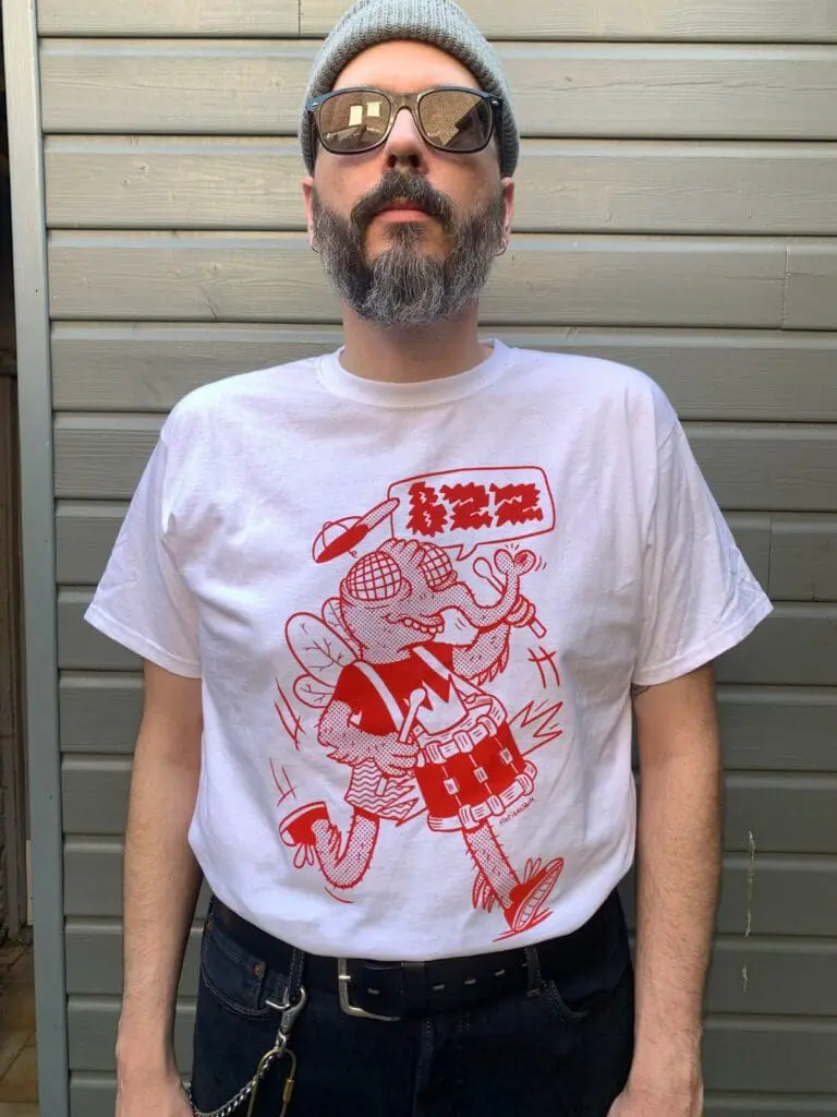 un homme porte un t shirt avec une mouche rouge qui joue de la batterie