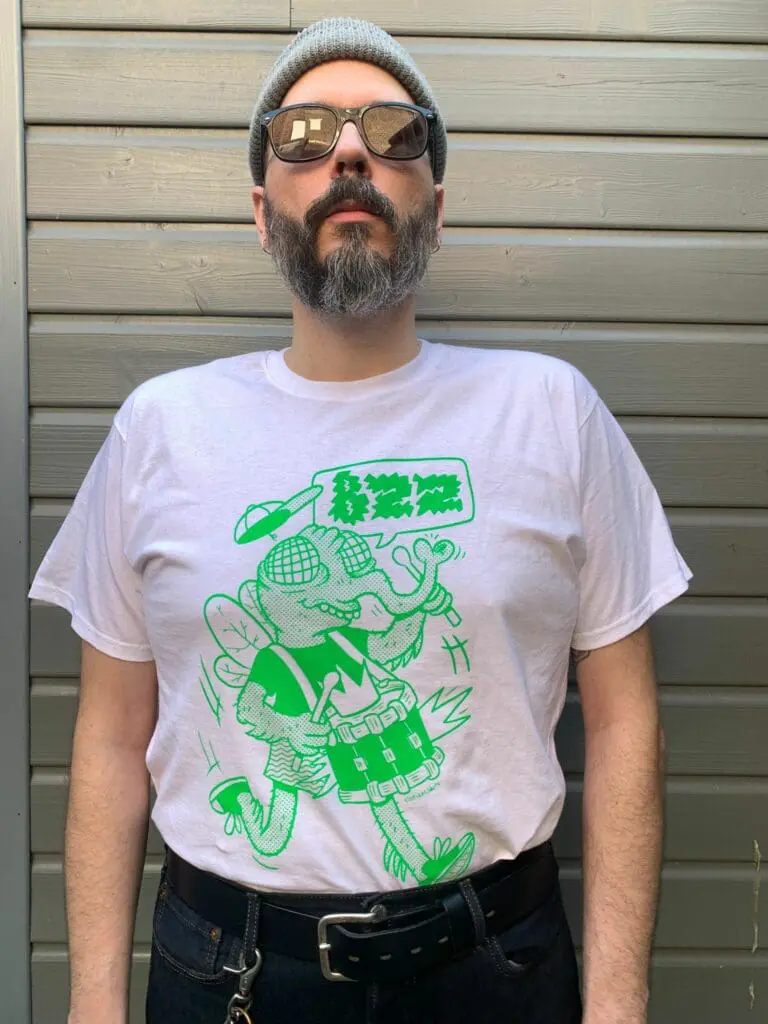 un homme porte un t shirt avec une mouche verte qui joue de la batterie