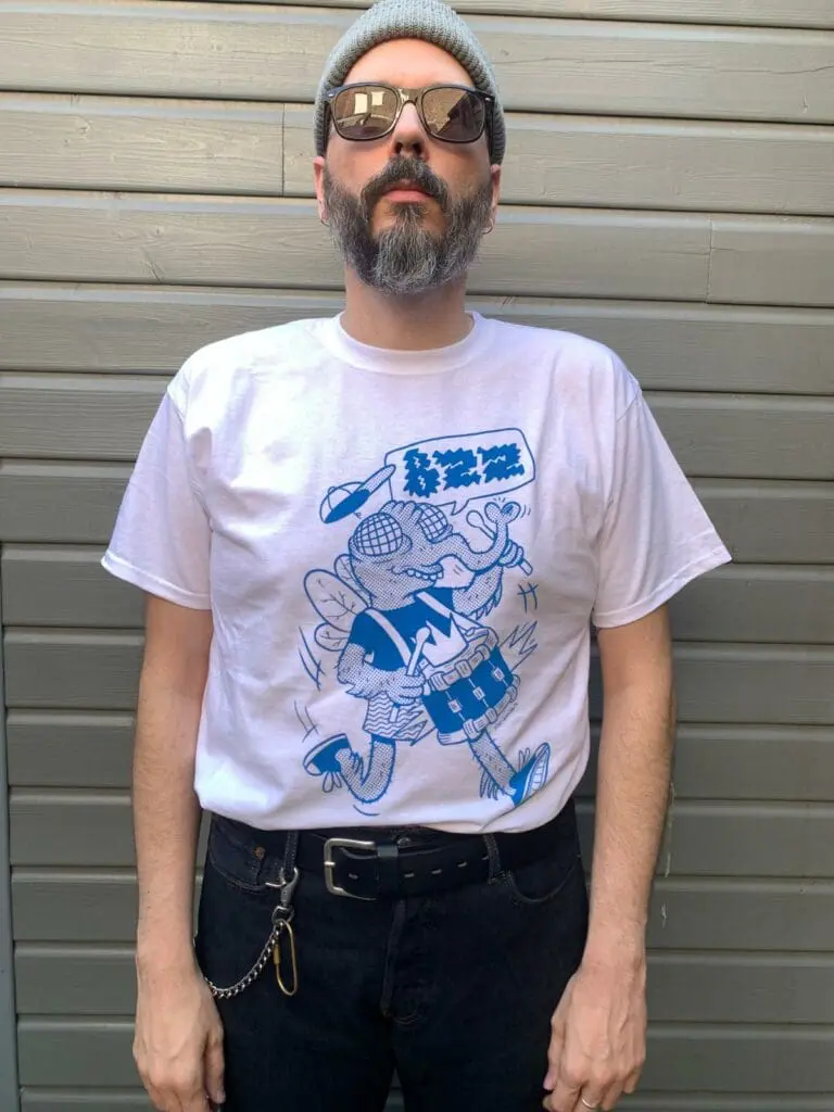 un homme porte un t shirt avec une mouche bleue qui joue de la batterie