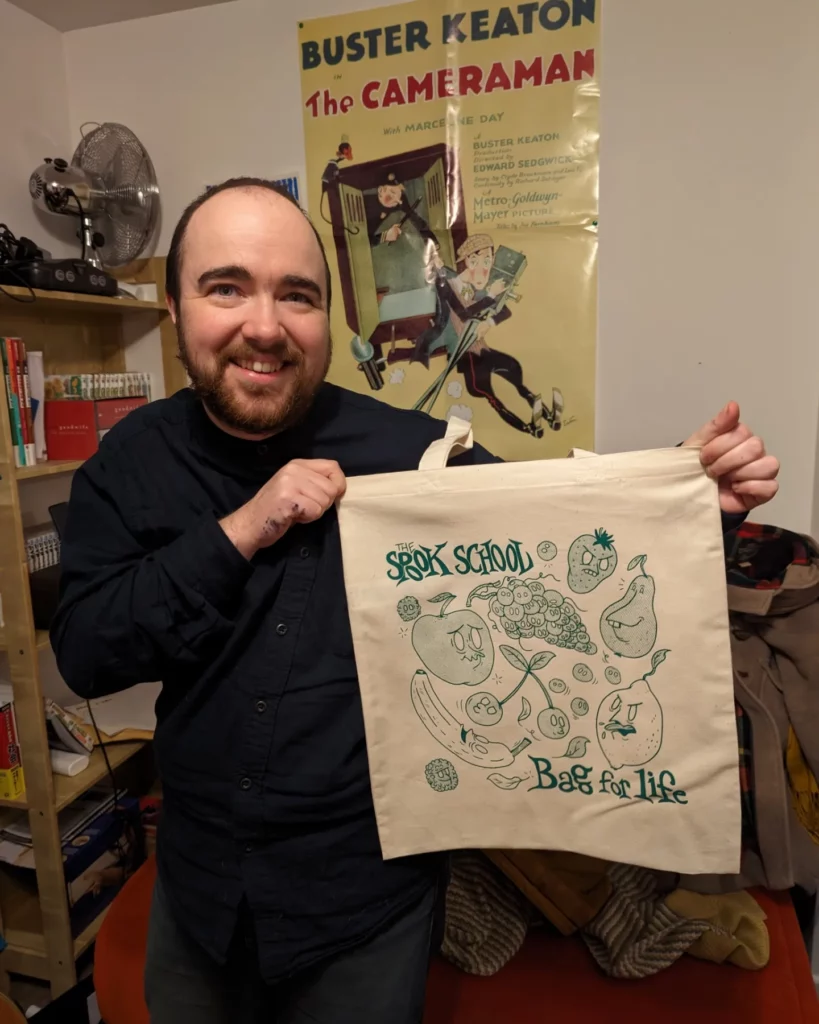 Un tote bag du groupe the spook school, illustré par plein de légumes et porté par une personne très souriante