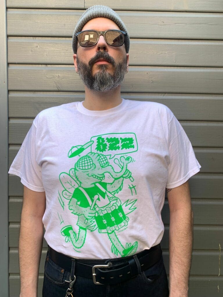 un homme porte un t shirt avec une mouche verte qui joue de la batterie
